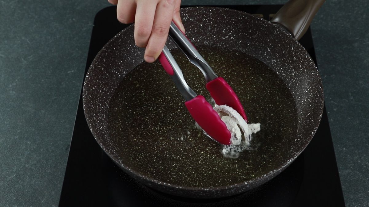 tongs putting onions into hot oil in skillet