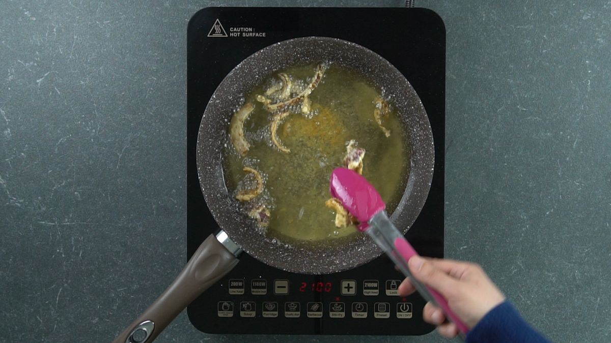 onions being removed from hot oil with pink tongs