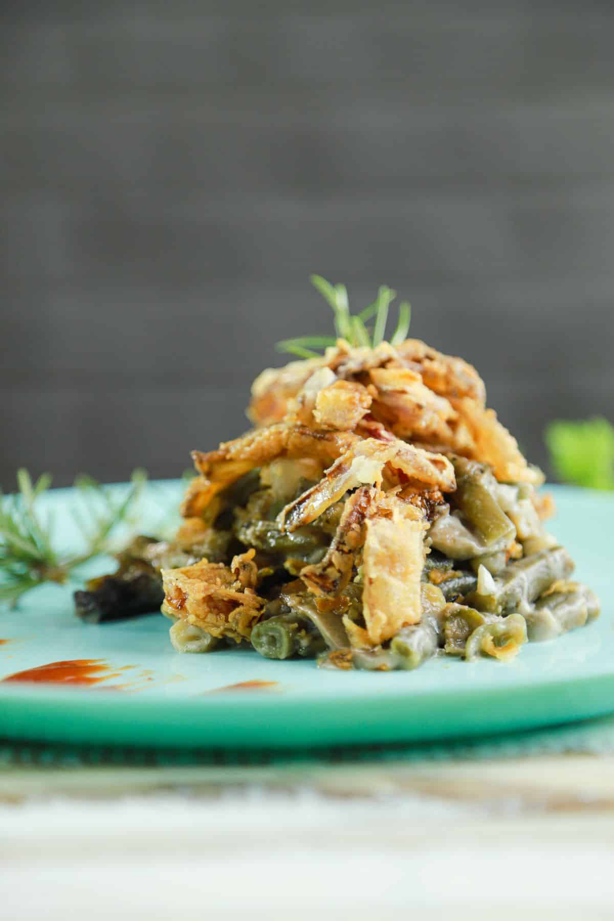 teal plate of green bean casserole on light wood table with gray background