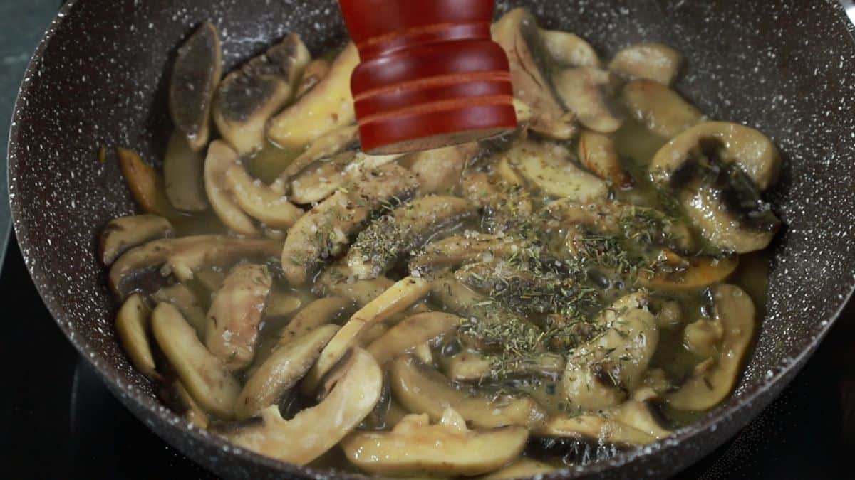 cracking pepper over mushrooms while they cook in skillet