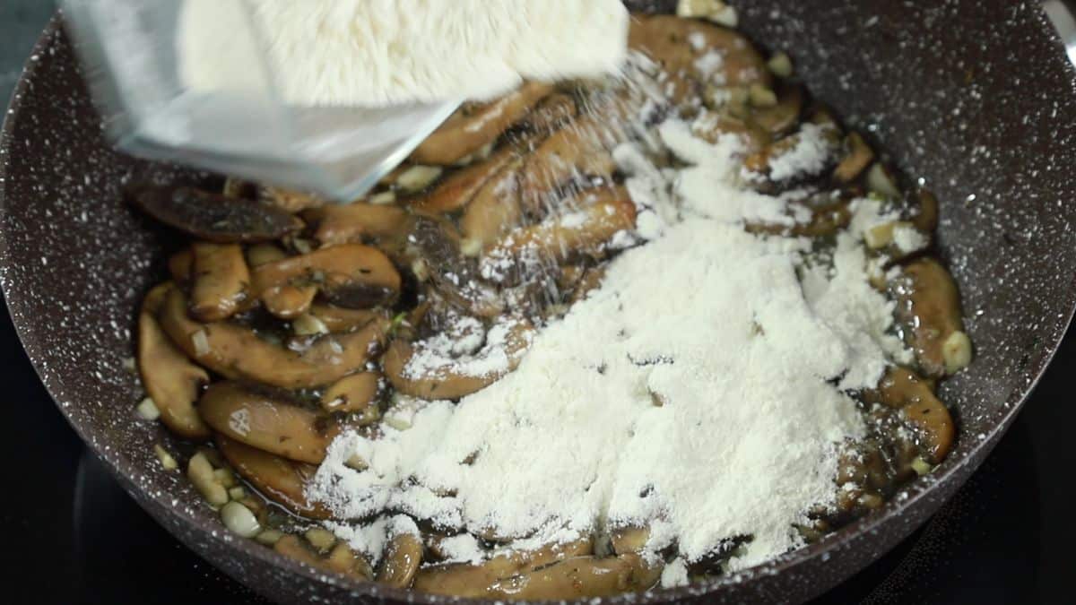 flour being poured into skillet with mushrooms