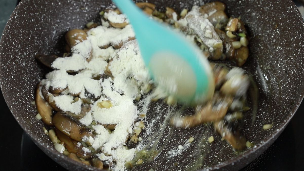 blue spoon stirring flour into mushrooms