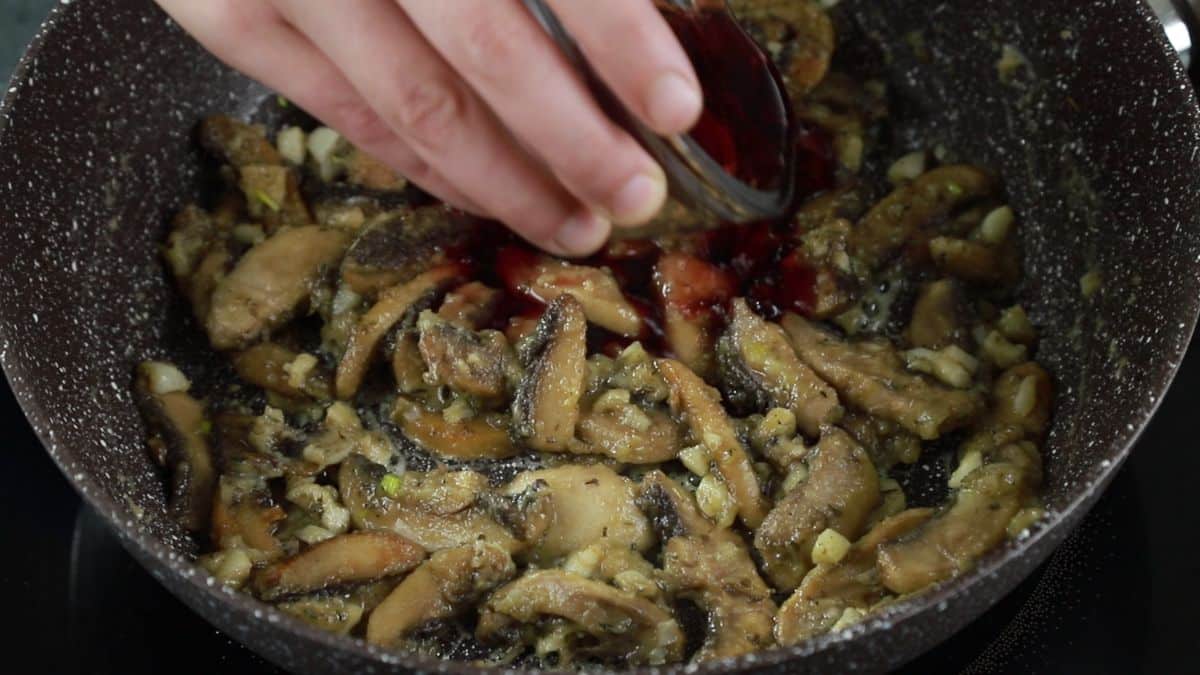 red wine being poured into skillet of cooked mushrooms