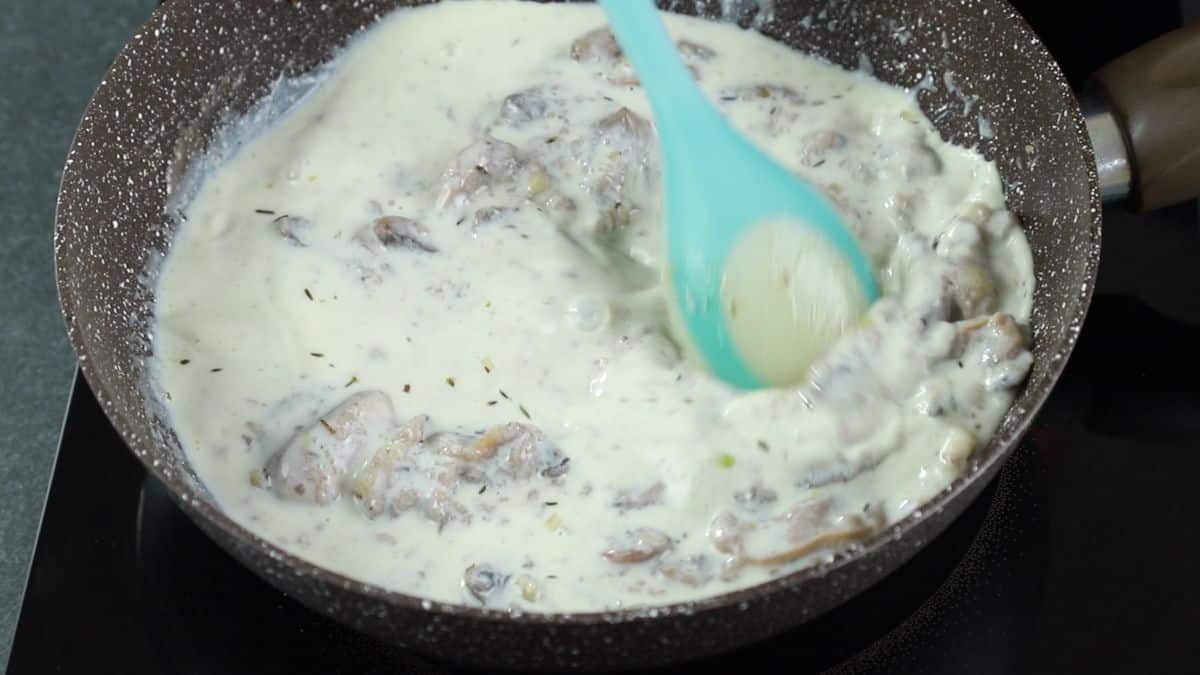 blue spoon stirring milk into skillet of mushrooms