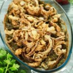 oval dish of green bean casserole on table with fresh herbs