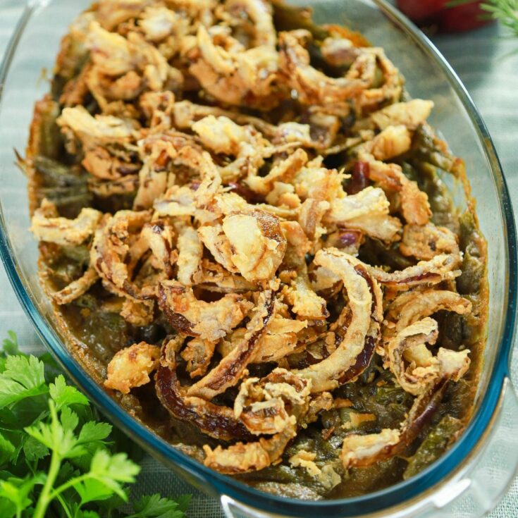 oval dish of green bean casserole on table with fresh herbs