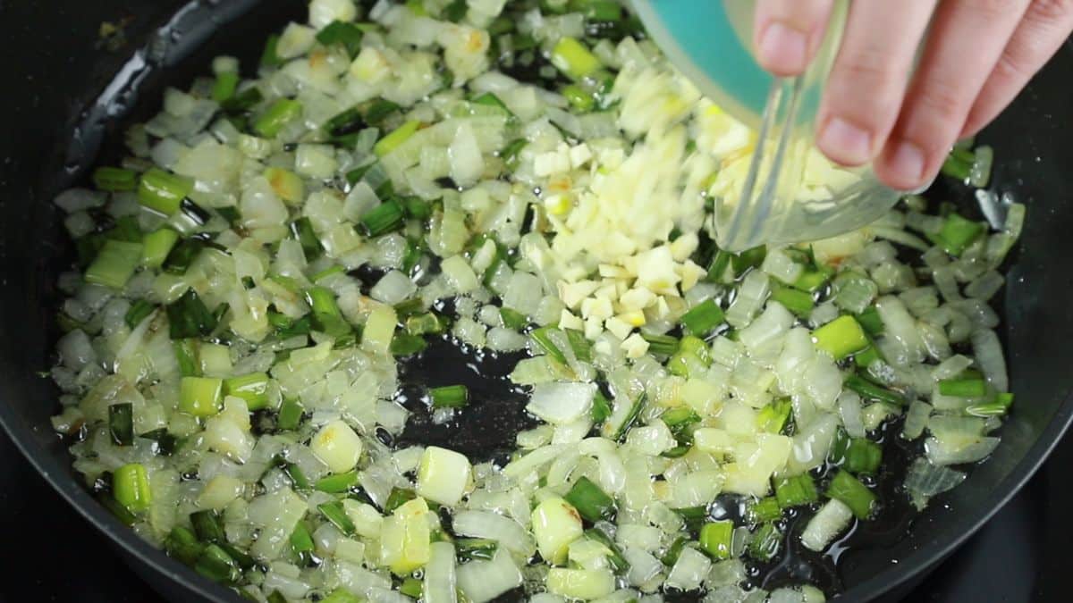 minced garlic being added to skillet of onions