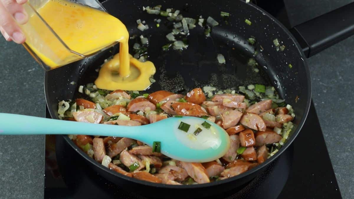 eggs being poured into skillet by pork sausage
