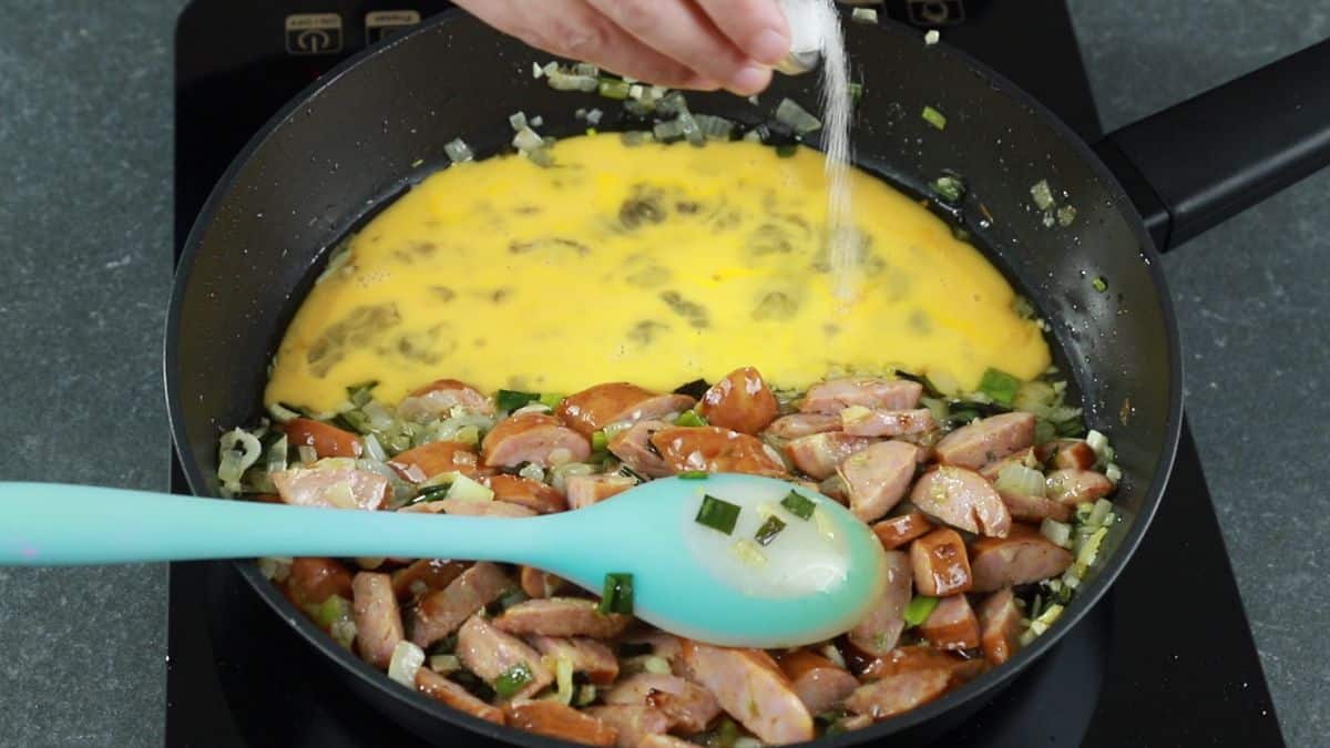 eggs being salted in skillet by sausage and onions