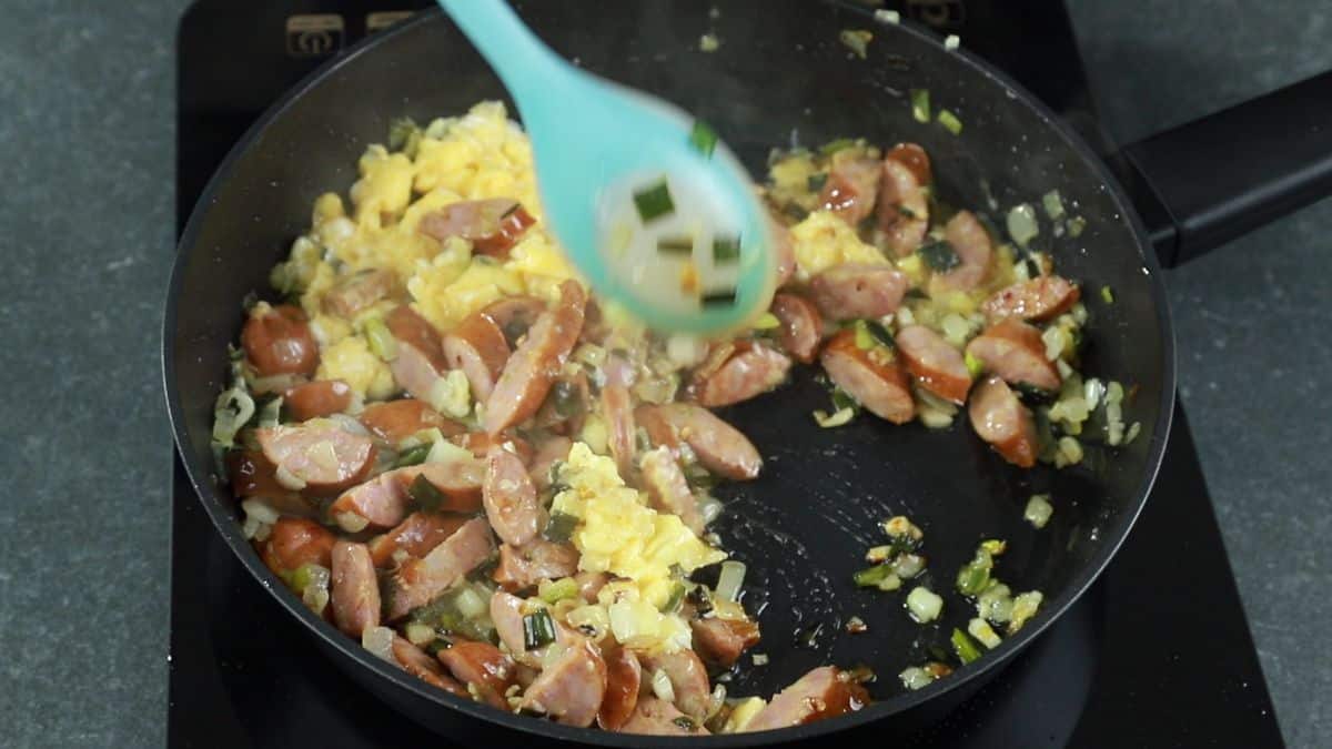 blue spoon stirring eggs with pork and onions