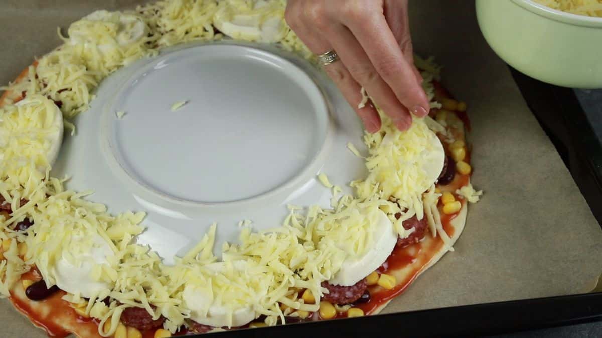 hand sprinkling cheese on pizza dough by plate
