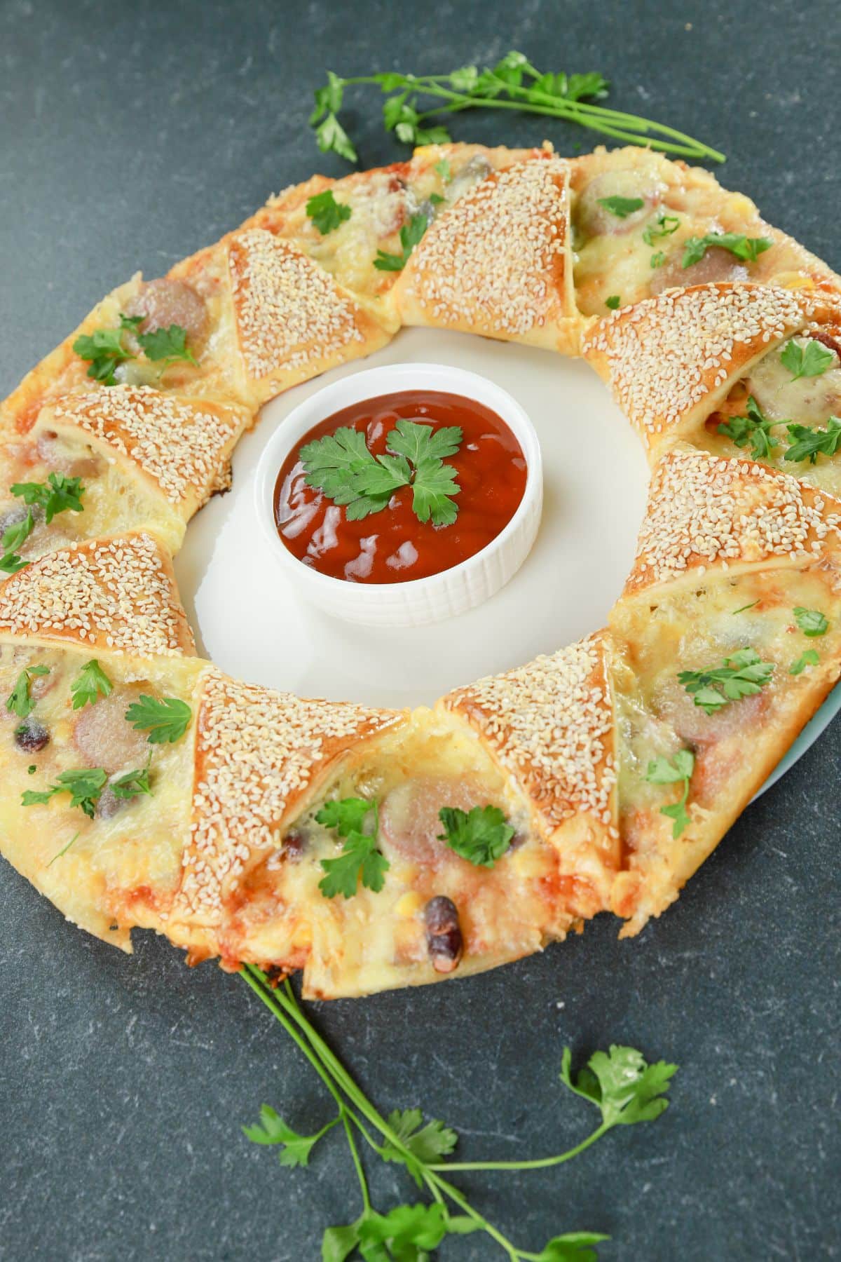 pizza ring with parsley on top and bowl of sauce in center