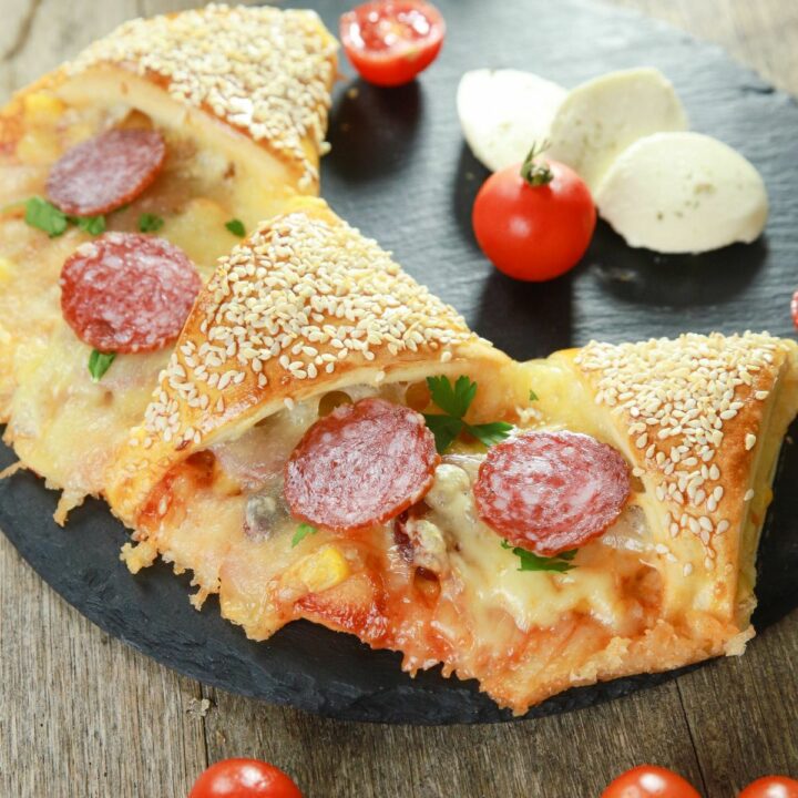 pizza ring topped with salami on plate with cherry tomatoes and mozzarella balls