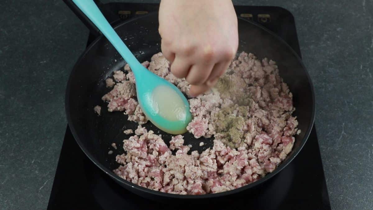 light blue spoon stirring ground meat in skillet
