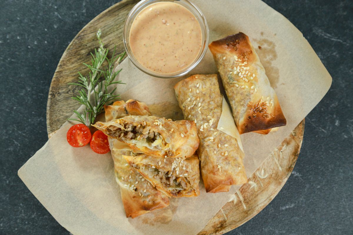 image looking down on plate of eggrolls with peppers and bowl of sauce on the side