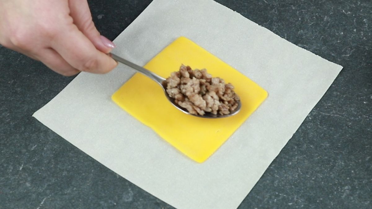 spoon of meat being added to eggroll wrapper on top of cheese