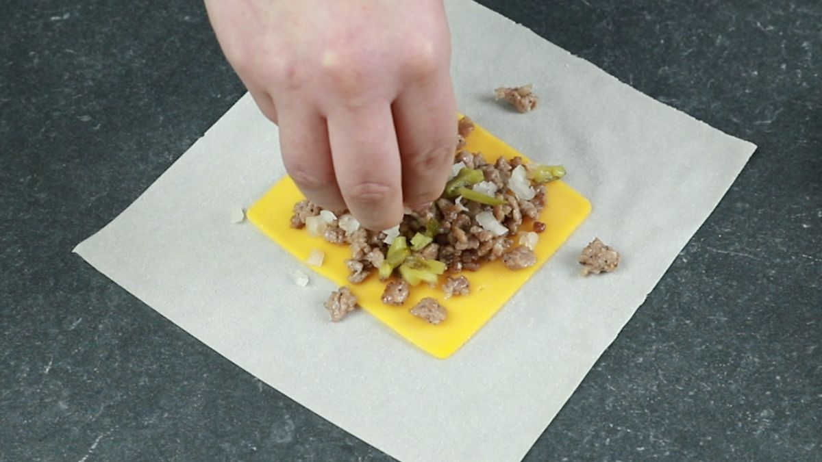onions and pickles being added to eggroll wrapper on top of ground beef