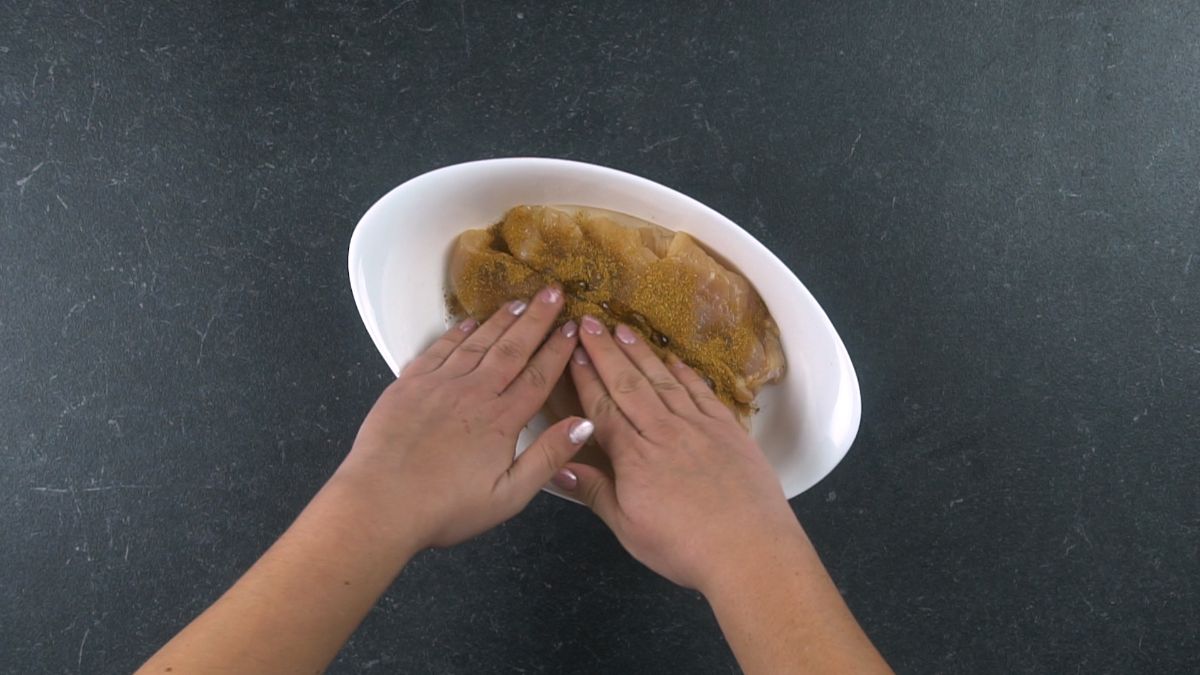 hands seasoning chicken breasts in white plate