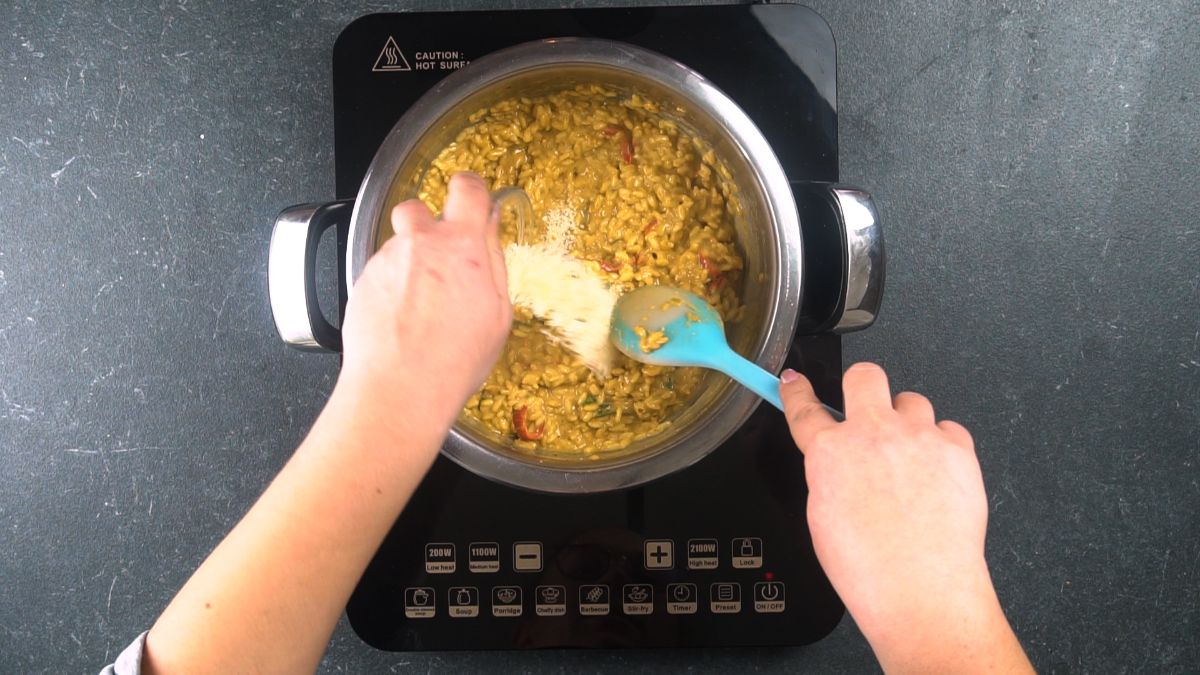 butter being added to orzo in stockpot on black hot plate