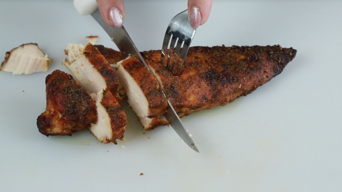 hand cutting chicken with knife on white cutting board