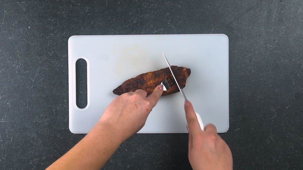 chicken on white cutting board being cut with a knife