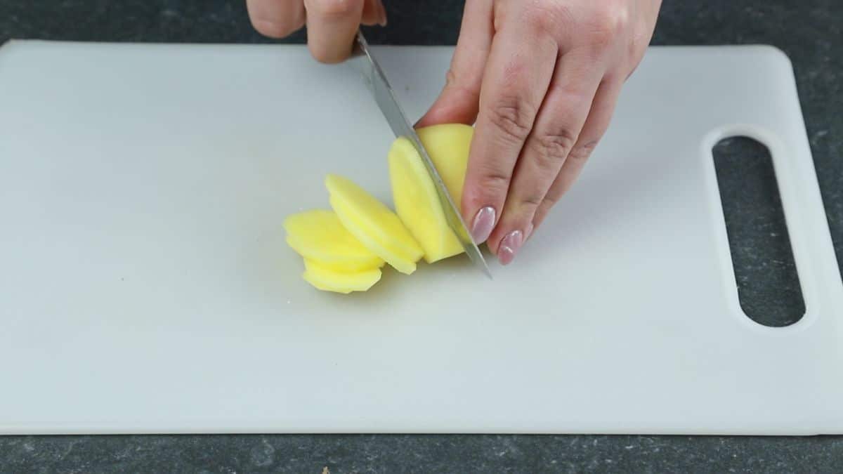 hand slicing potatoes on white cutting board