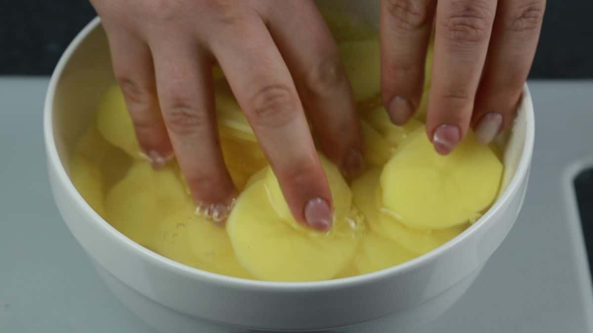 hands pushing potato slices into bowl of water
