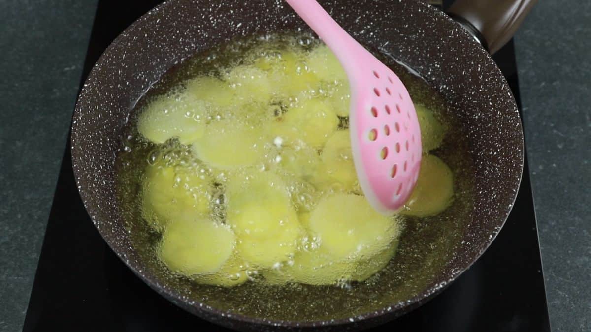 potato slices in black skillet of oil with pink spoon
