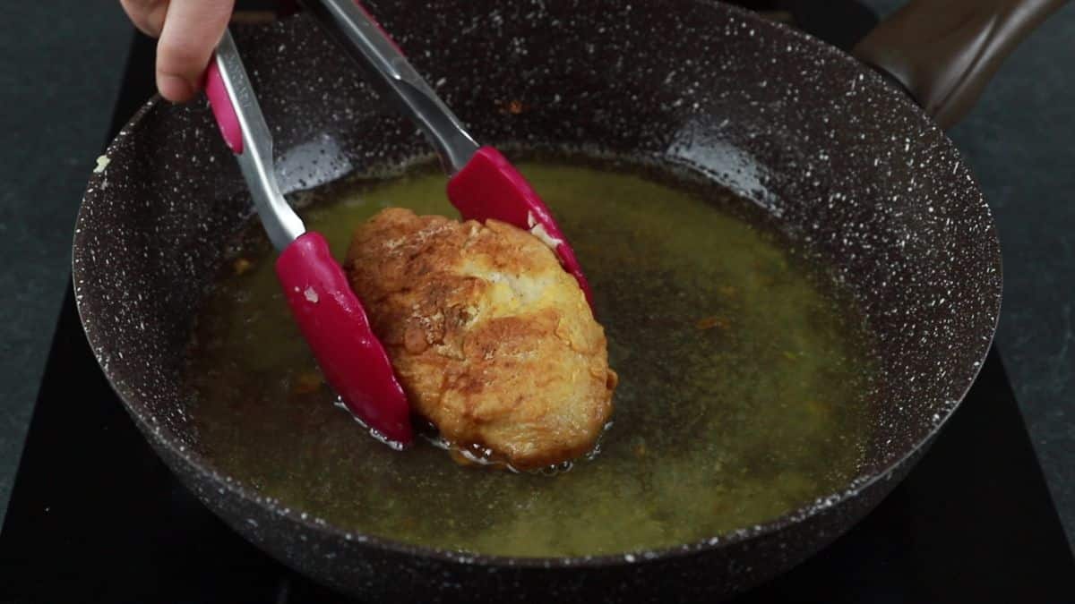 pink tongs lifting fried chicken out of skillet