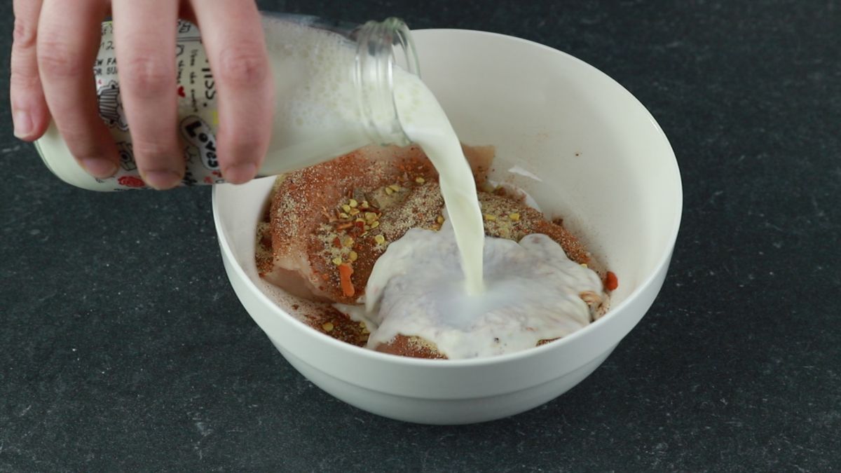 milk being poured into bowl with seasoned chicken
