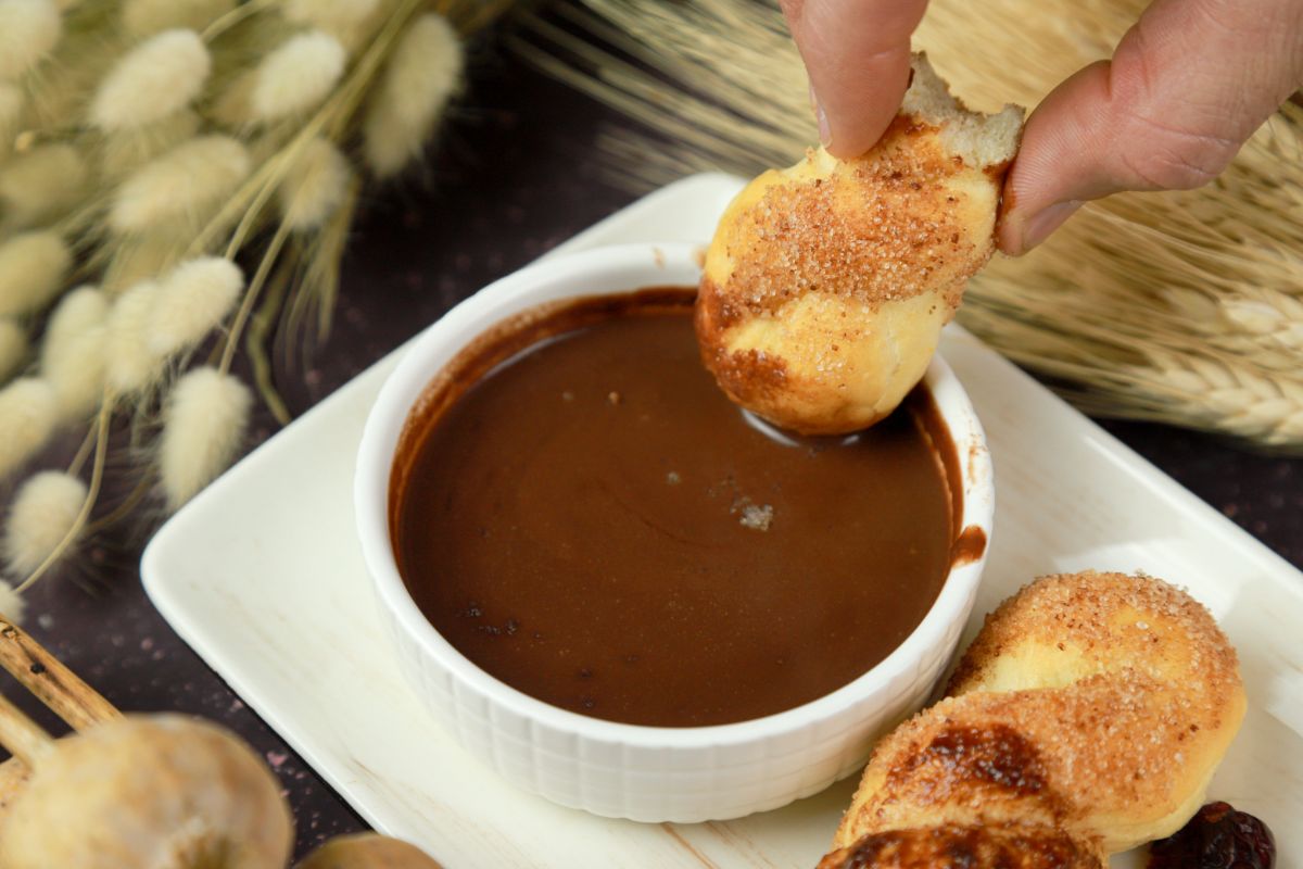 hand dipping donut into chocolate sauce