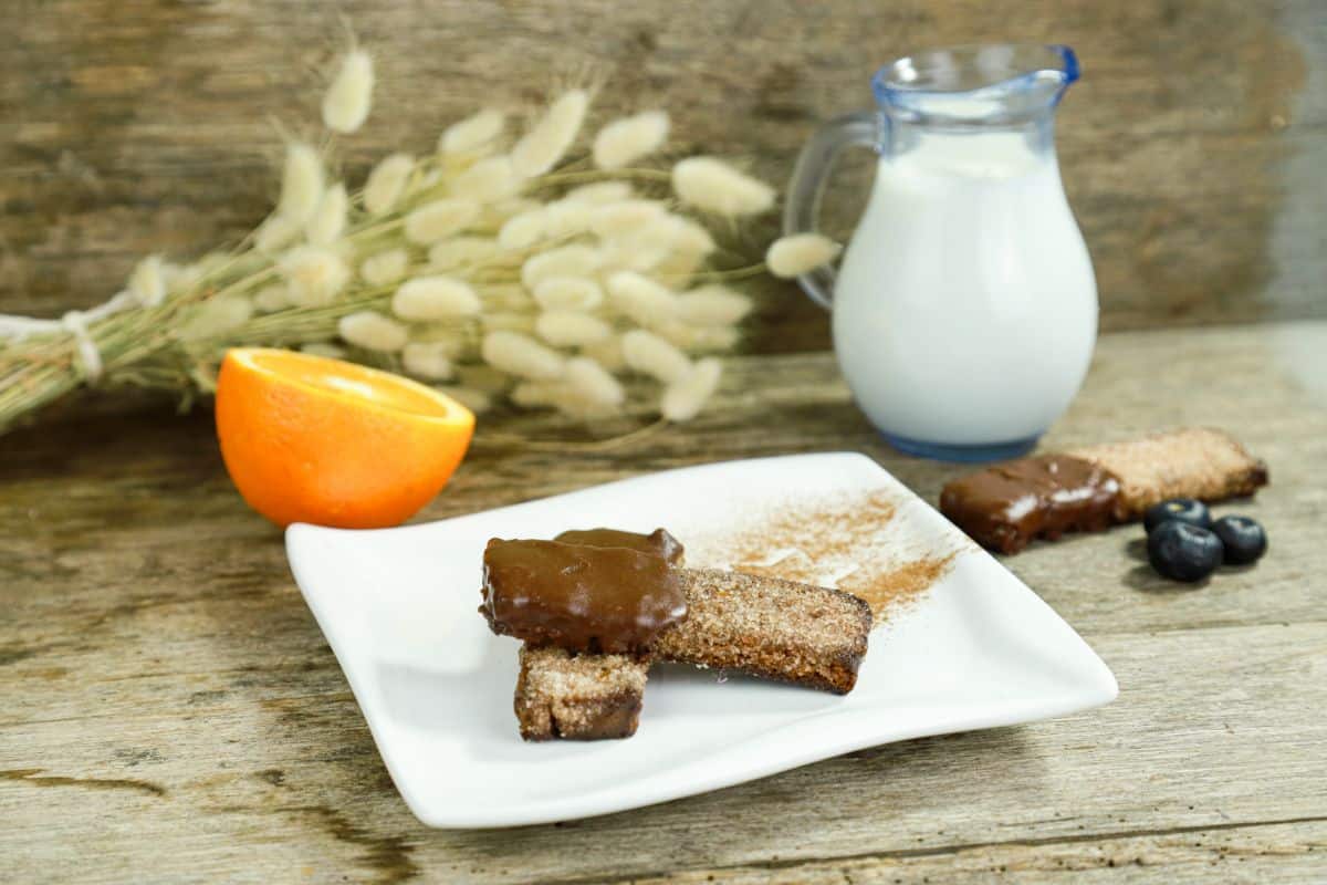 bottle of milk and half an orange beside white plate holding bread with cinnamon sugar and chocolate sauce