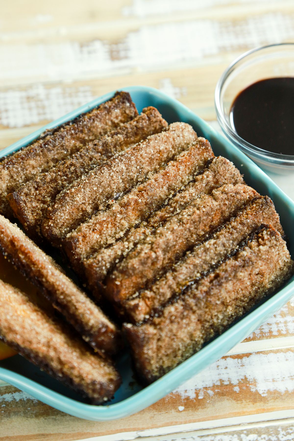 cinnamon breadsticks stacked together in teal bowl by glass bowl of chocolate sauce