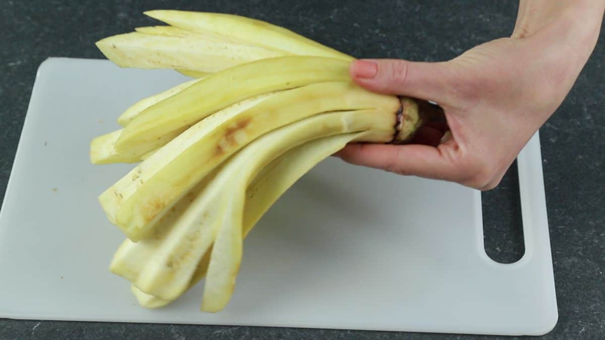 hand holding peeled sliced eggplant above cutting board
