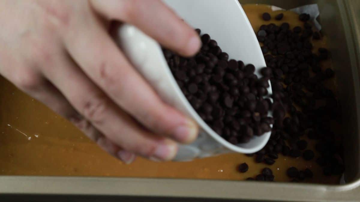 white bowl of chocolate chips being poured over milk in baking dish