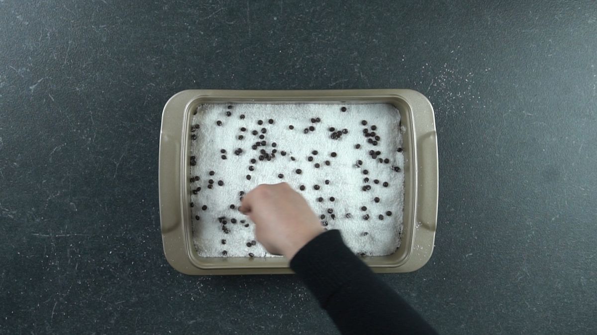 chocolate chips being spread over top of hello dolly bars