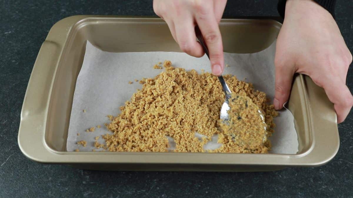 graham cracker crumbs being pressed into bottom of baking dish