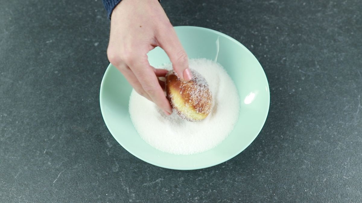 rolling fried donut in sugar