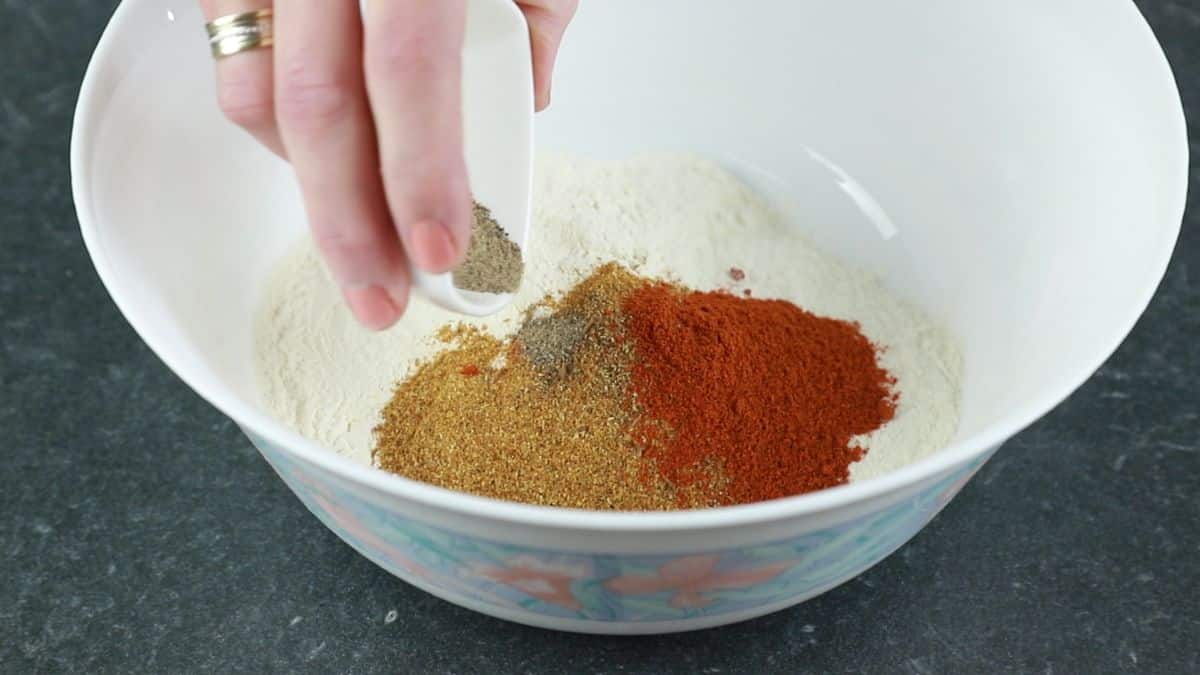 pepper being added to white bowl of flour