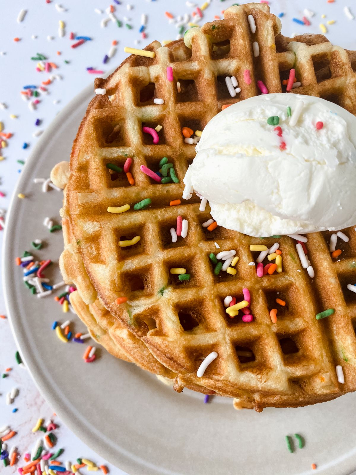 stack of birthday cake waffles on white plate topped with ice cream and sprinkles