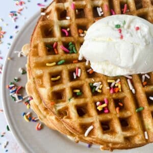 stack of birthday cake waffles on white plate topped with ice cream and sprinkles
