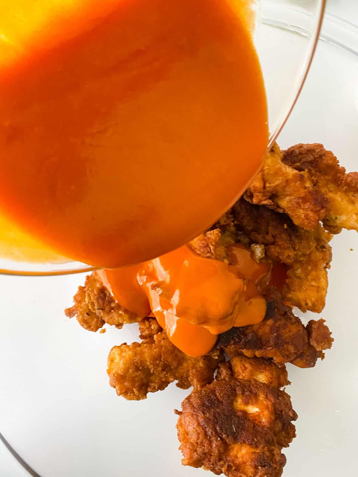 buffalo sauce being poured over fried chicken pieces