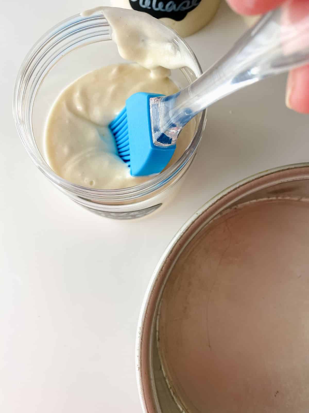 blue silicone pastry brush dipping into jar of cake release