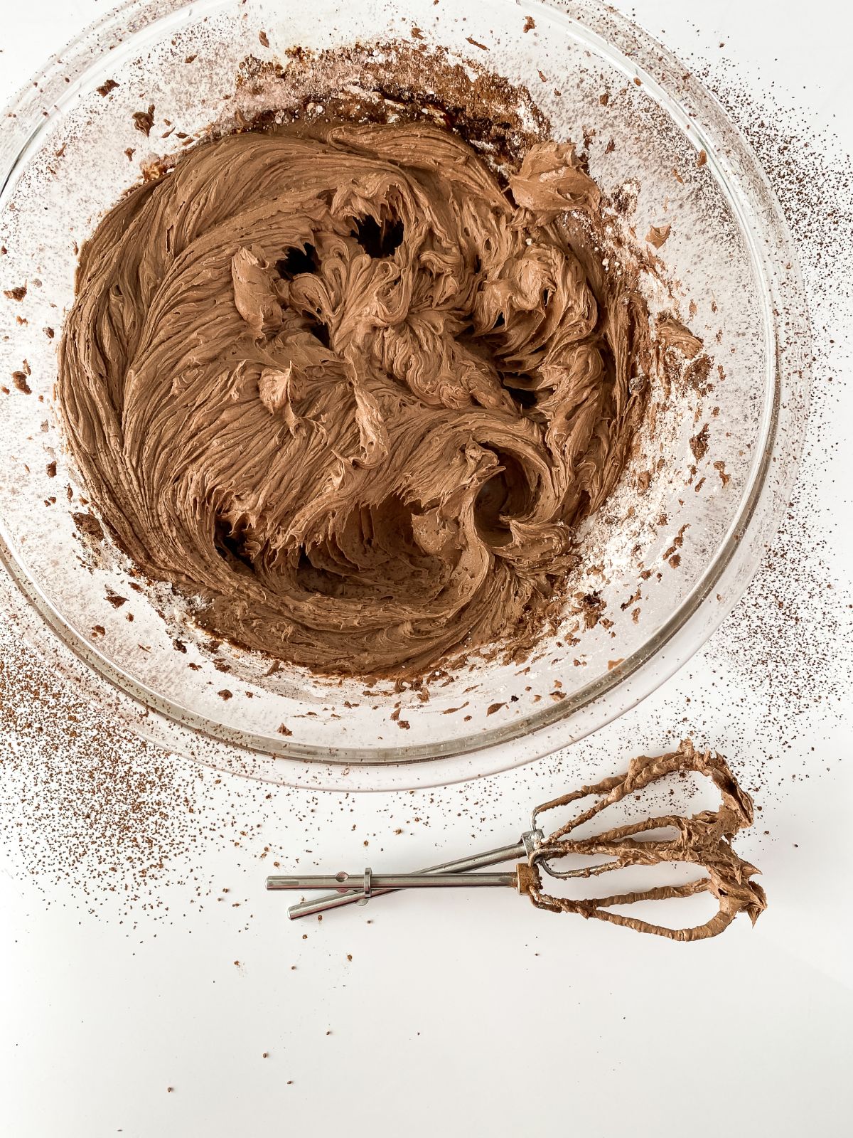 bowl of chocolate frosting on table with dusting of cocoa beside bowl