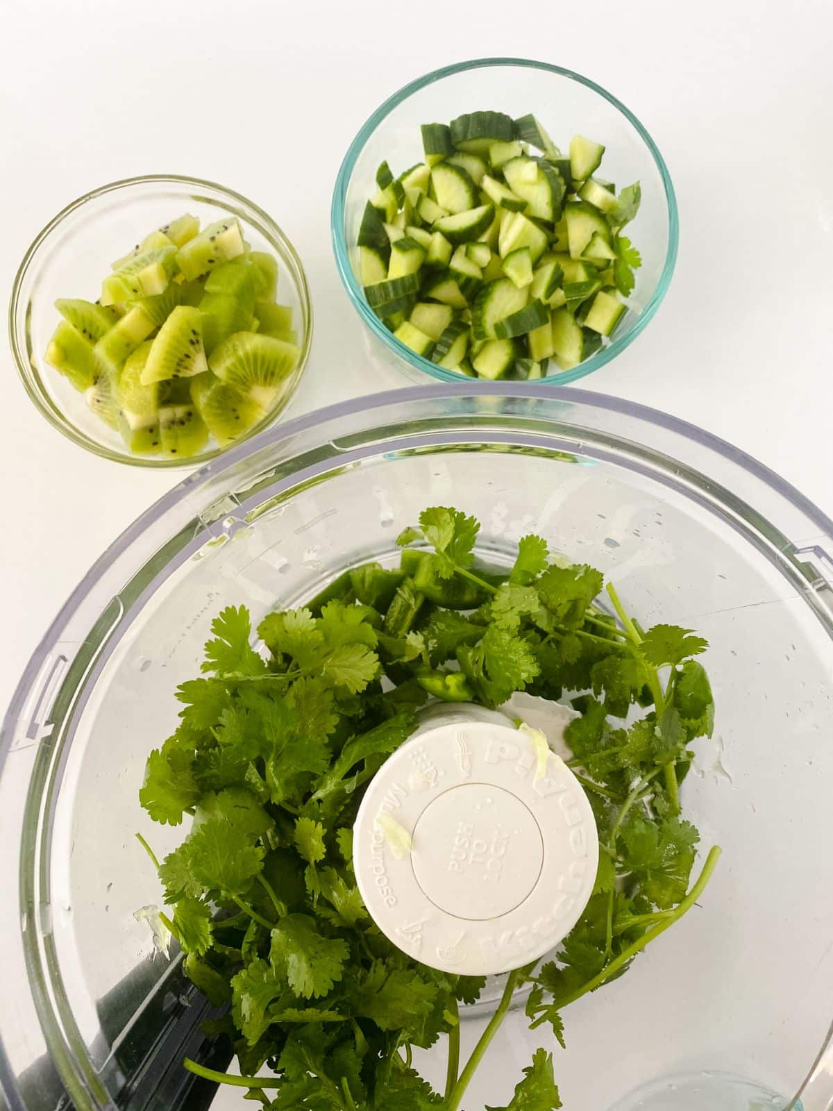 cilantro in food processor with bowls of cucumber on side