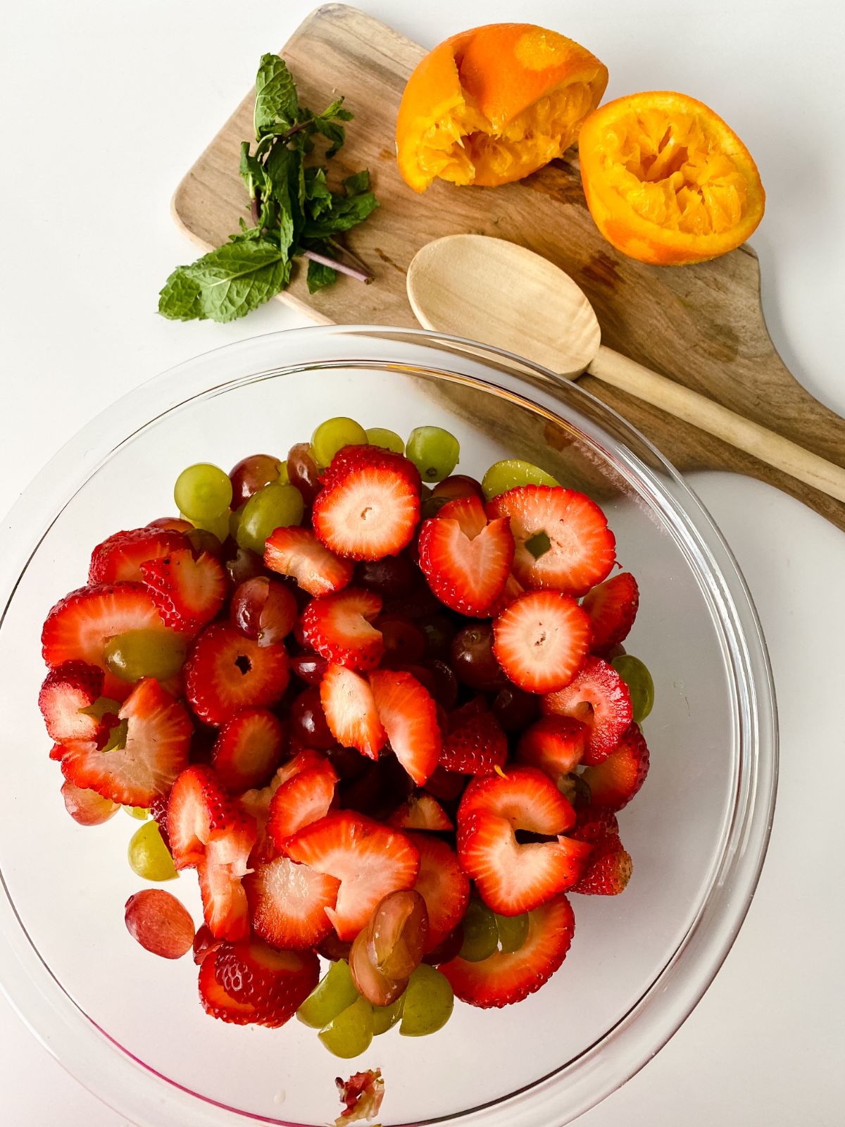 strawberry slices in large glass bowl with orange halves on cutting board on the right