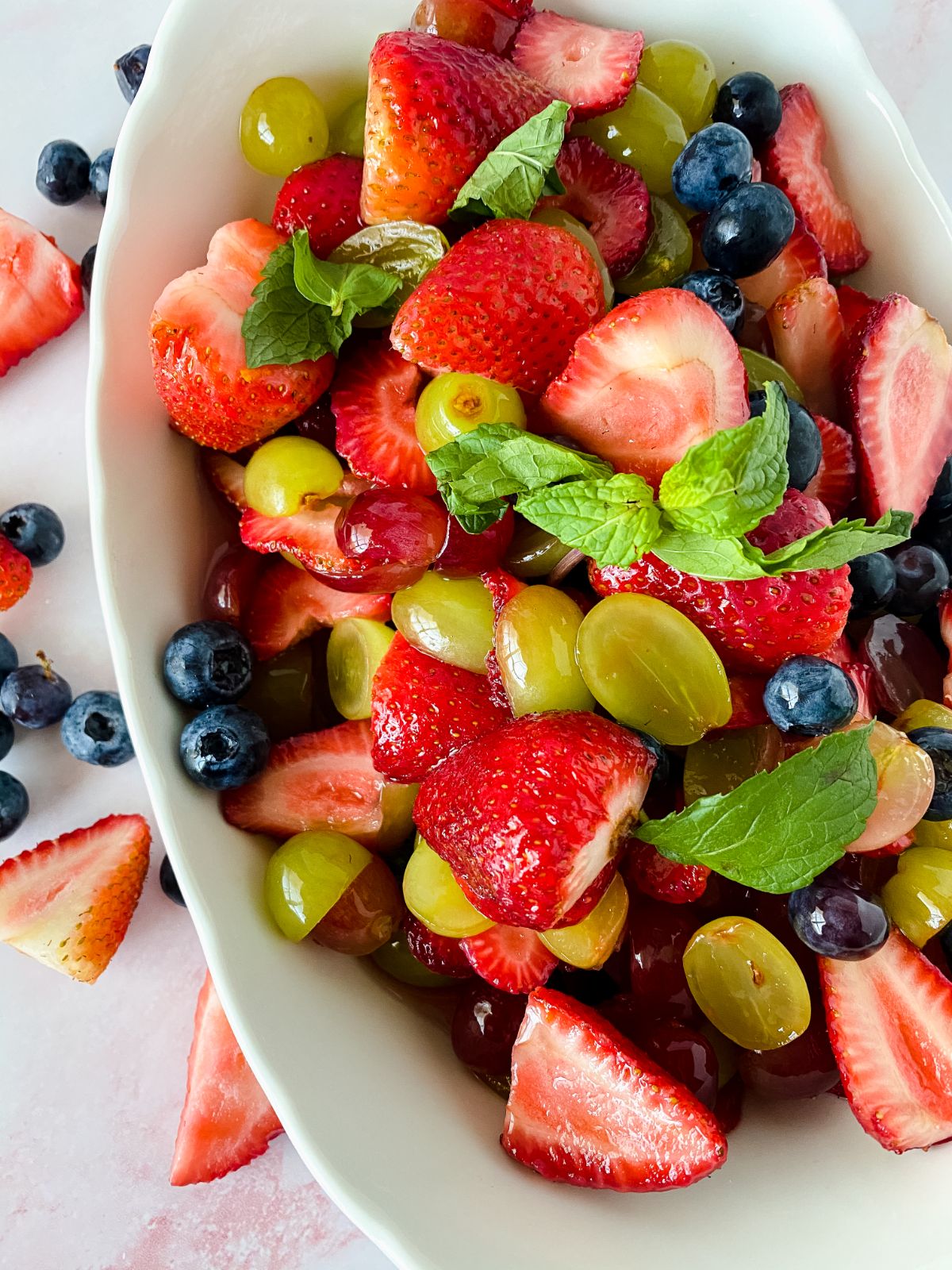 white bowl of fruit salad with strawberries blueberries and grapes