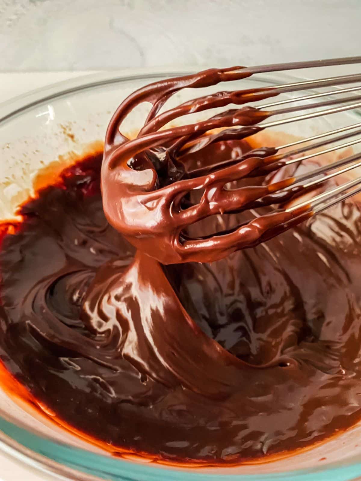 chocolate ganache in glass bowl with whisk above