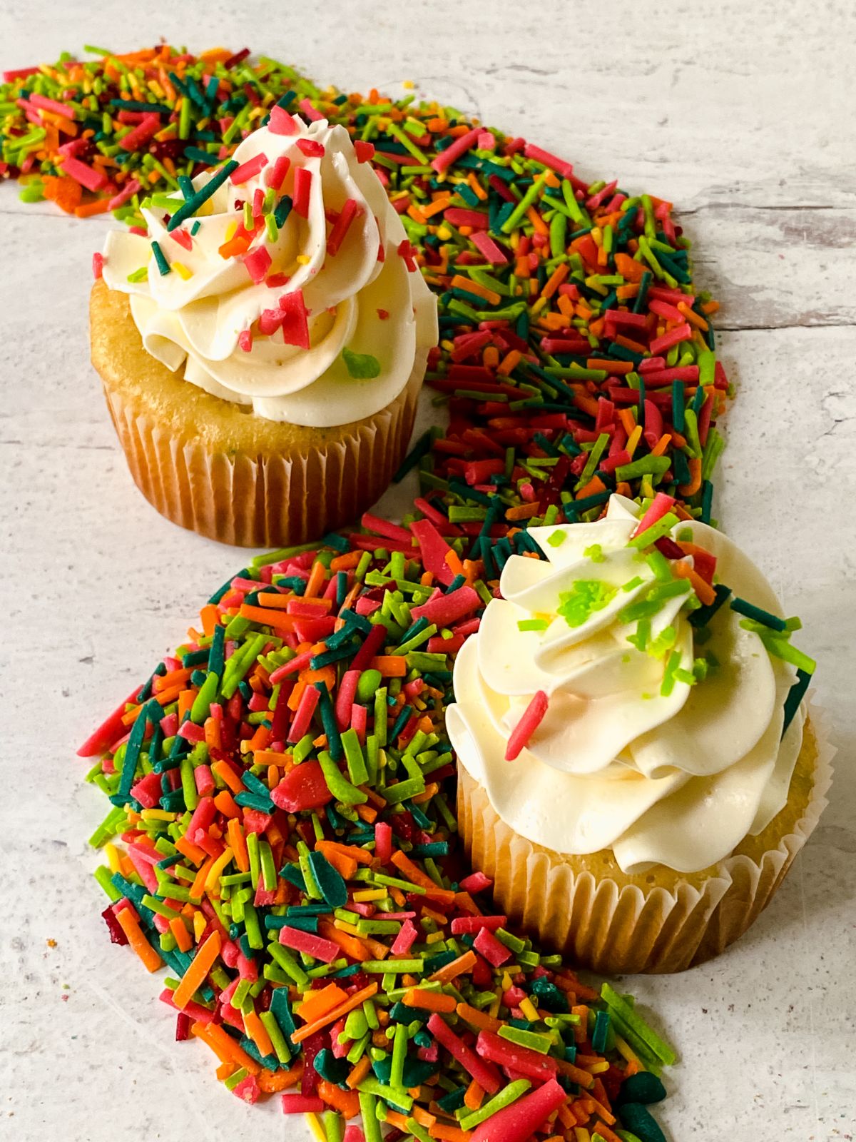 two cupcakes with white icing and sprinkles on table 