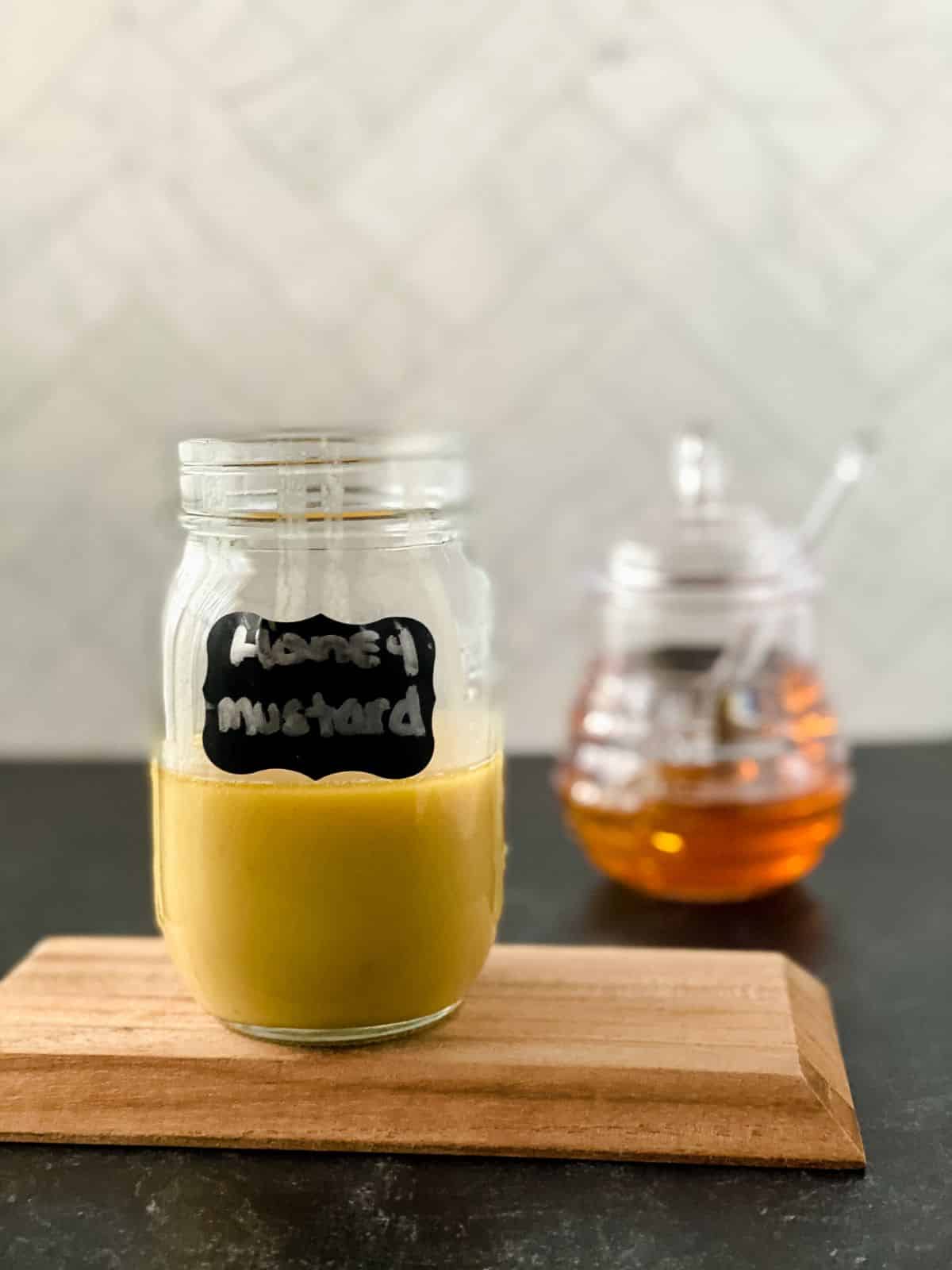 jar of honey behind jar of honey mustard on top of cutting board